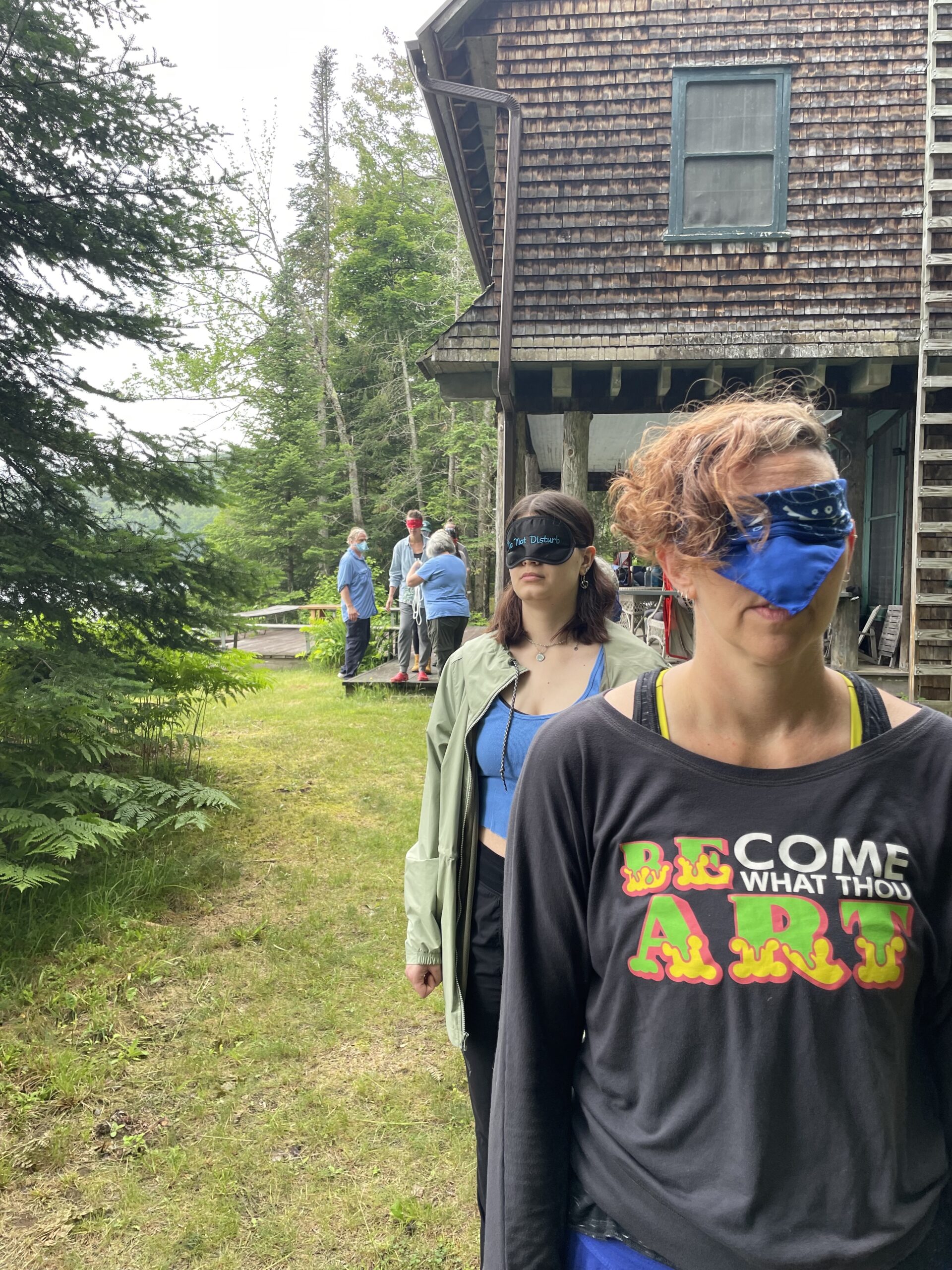 Two people blindfolded and standing outside in front of a house.