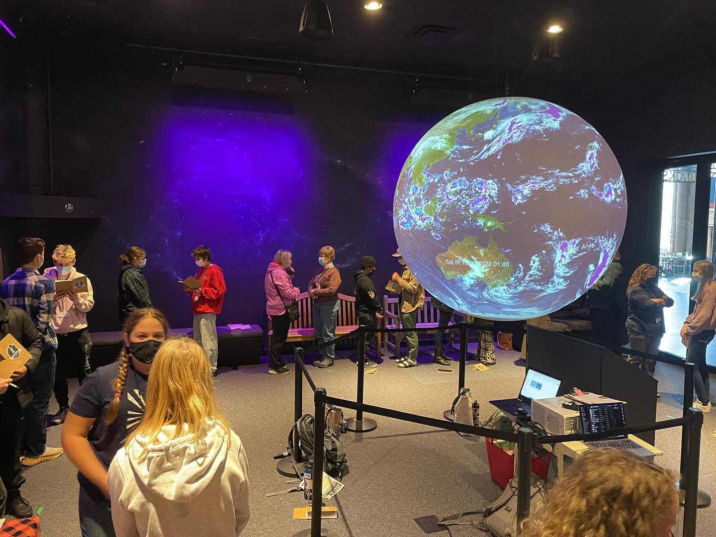 Many people standing and talking around an exhibit.